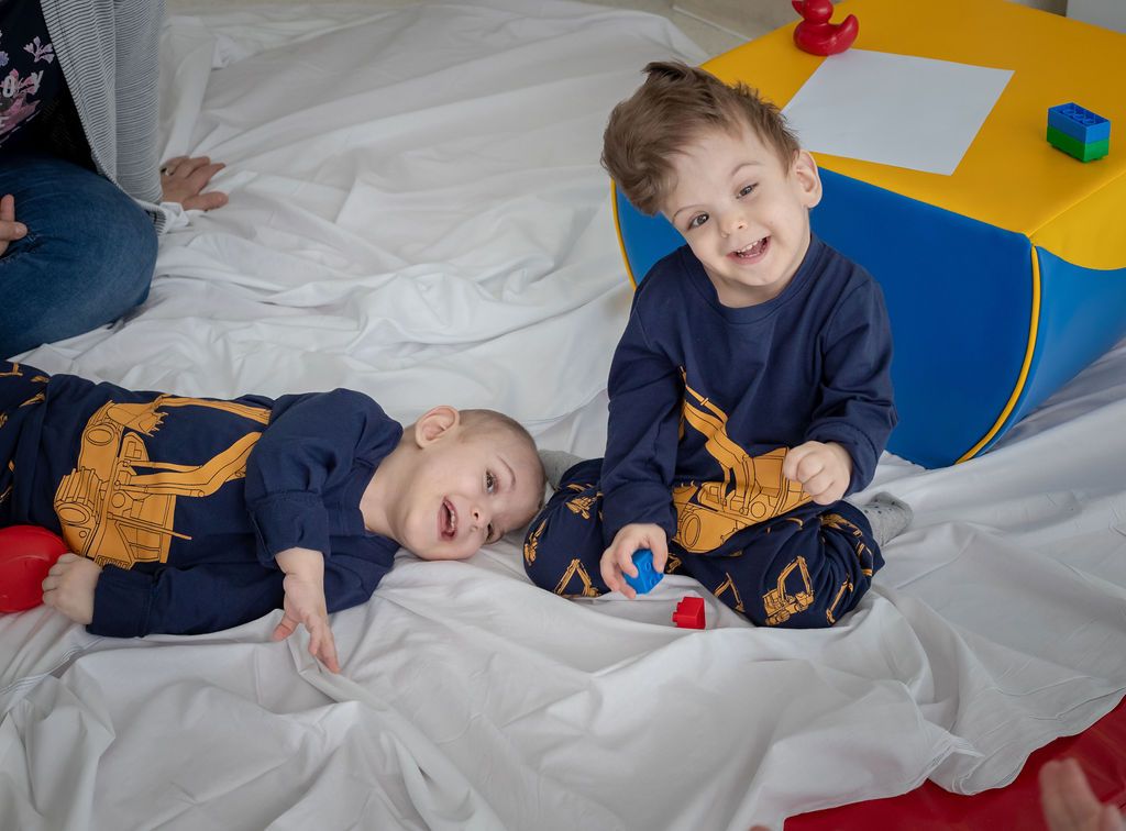 Yigit and Derman, two craniopagus twins, smile happily post their separation operation. They are sitting on a bed.