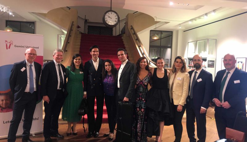 Attendees at the Gemini Untwined fundraiser, including Dr. Jeelani, pose for a group photograph. They are in the Wellcome Collection. A staircase with a red carpet lies in the background.